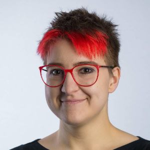 Masha Budryte smiling, with red hair and glasses